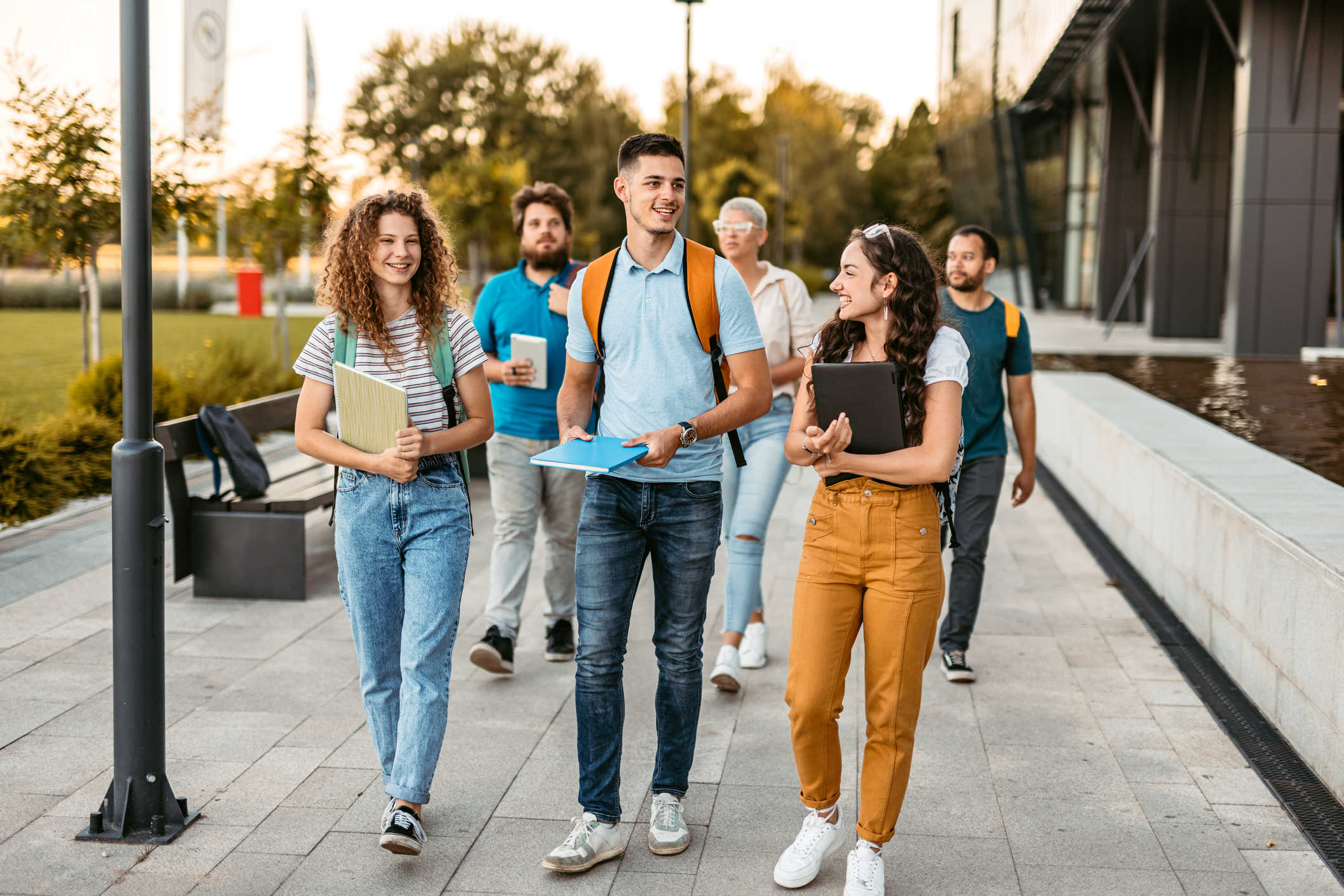 Students Walking On The University Campus Group of friends walking on the university campus, holding books and notebooks.